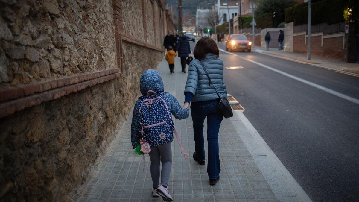 Una mujer lleva de la mano a un niño a clase.