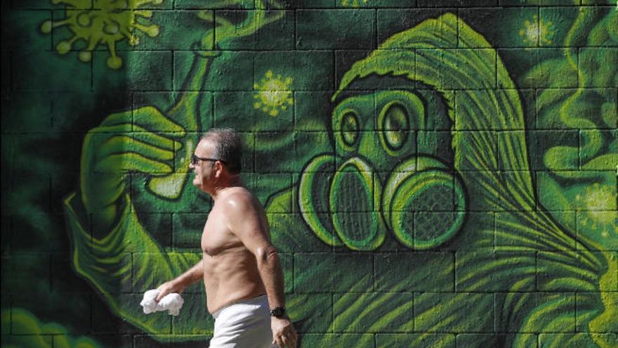 Un hombre camina ante un grafiti alusivo al coronavirus en Barcelona.