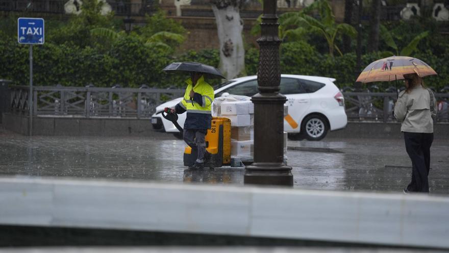 Varias personas se protegen de la lluvia con un paraguas en Sevilla.