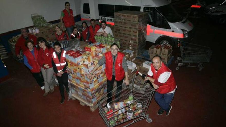 Arriba, varios de los voluntarios de la Cruz Roja de Avilés que hacen posible el reparto de alimentos posando tras la agotadora jornada. A la izquierda, entrega de uno de los lotes de comida. | mara villamuza
