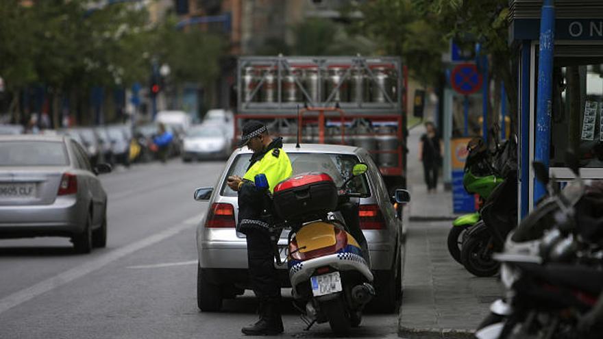 Un policía local de Alicante impone una multa este viernes a un coche mal estacionado en el centro de la ciudad