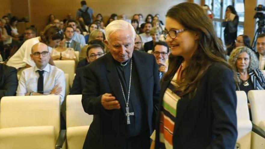 El cardenal Antonio Cañizares hace un gesto a la vicepresidenta del Consell, Mónica Oltra, antes de iniciar la conferencia.