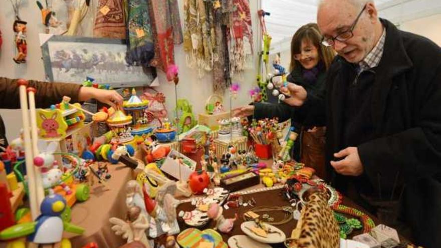 Dos clientes observan juguetes artesanales en un estand de la feria.  // G. Santos