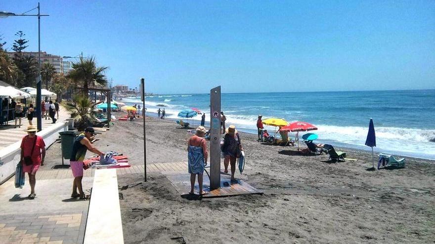 Torrox. Dos bañistas se quitan  la arena en una ducha de la playa de Ferrara.