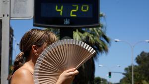 Una mujer se abanica mientras pasa por un termómetro de calle que marca 42 grados en Córdoba, este jueves.
