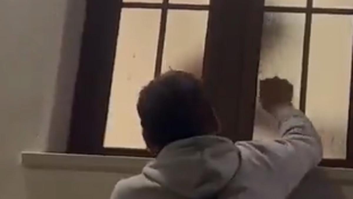 Un hombre golpea la ventana de una casa al paso de una procesión