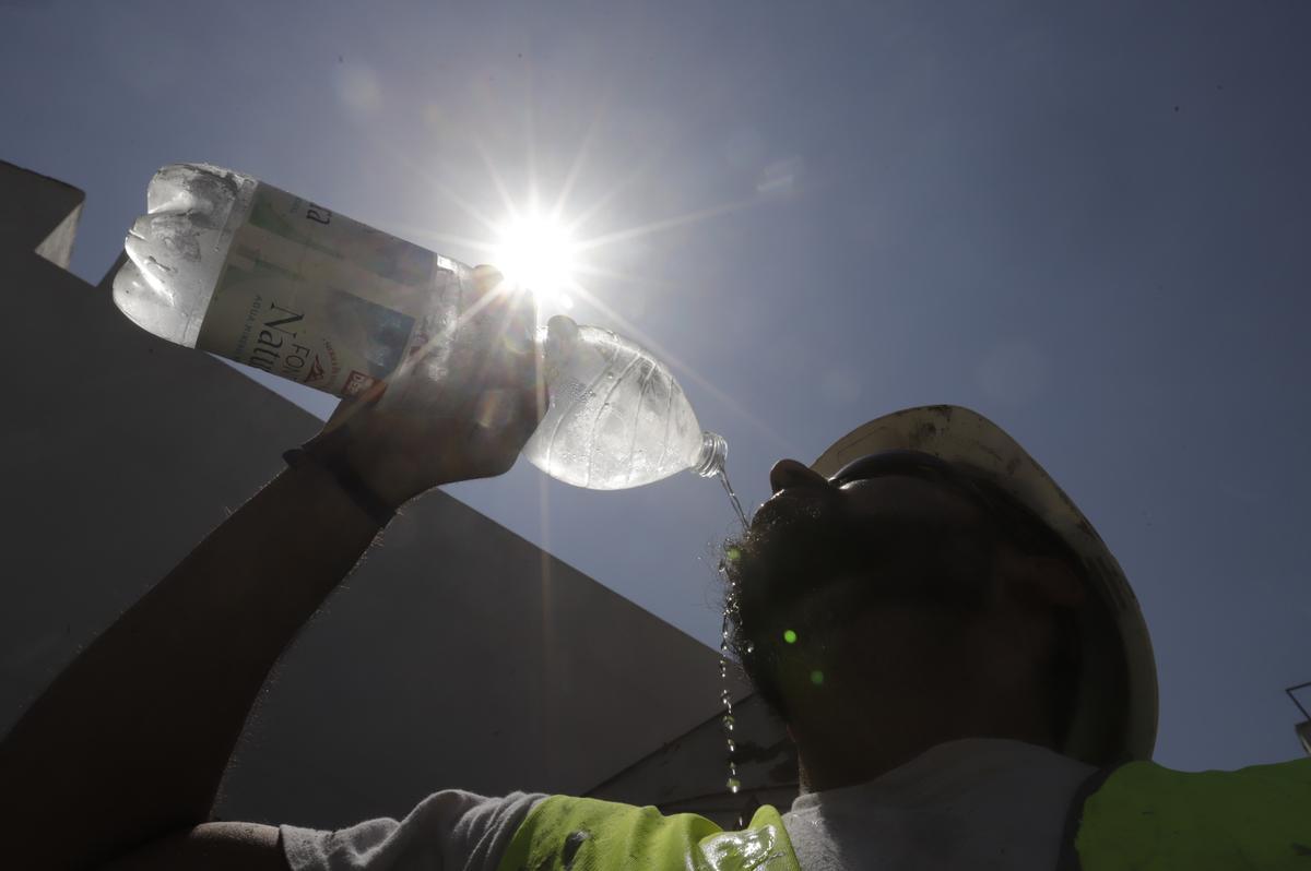 Un trabajador bebe agua fría durante su jornada laboral a pleno sol.