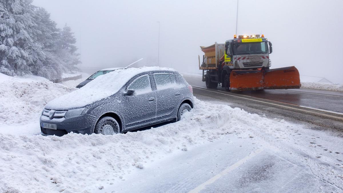 Un coche cubierto de nieve y una máquina quitanieves en la carretera de acceso al Puerto de Navacerrada.