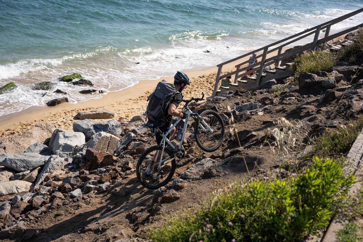 Un ciclista escalando el muro de piedras de la playa de Montgat (la escalera del fondo de la imagen está rota)