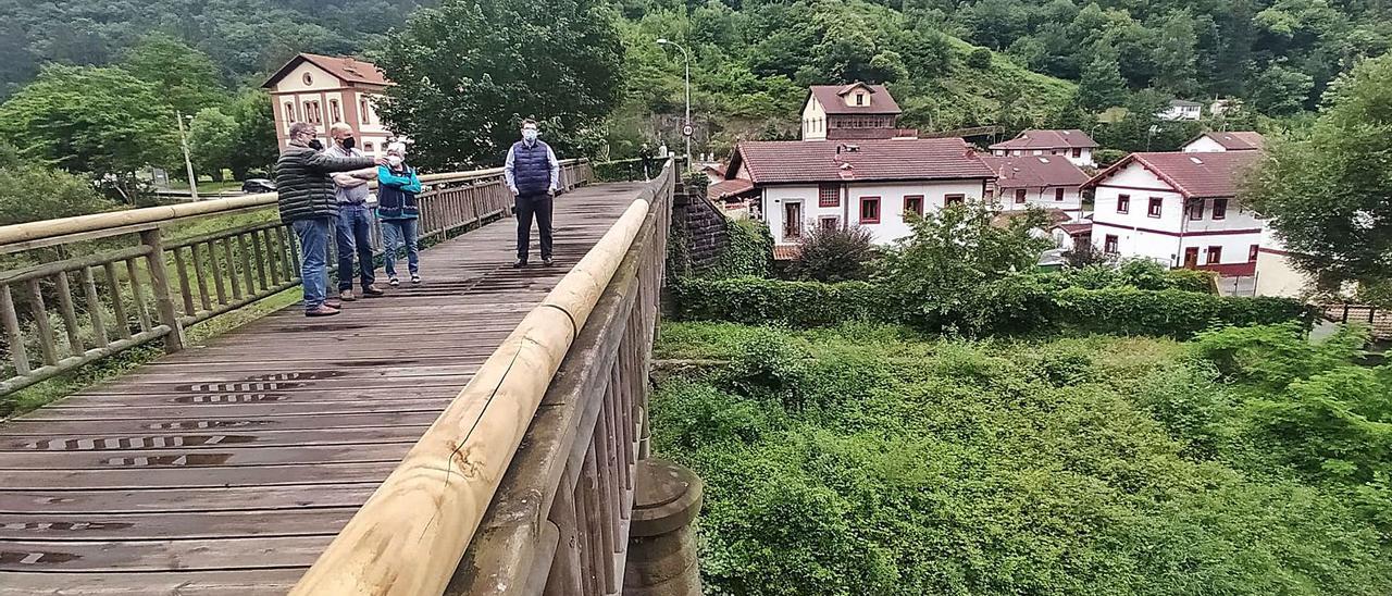 Por la izquierda, Fernando Muñiz, Miguel Palacios, Menchu Arias y el párroco Alfonso Abel, en el puente de Bustiello, con el poblado al fondo. | D. M.