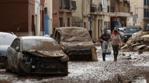 Vecinos de Paiporta trabajan en la limpieza de calles, locales y viviendas de la localidad junto a una montaña de vehículos arrastrados por la corriente, este viernes.