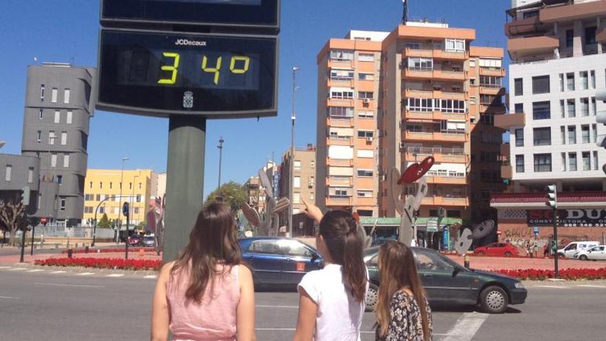 Tres jóvenes miran un termómetro que marca 34 grados, hoy en Murcia.
