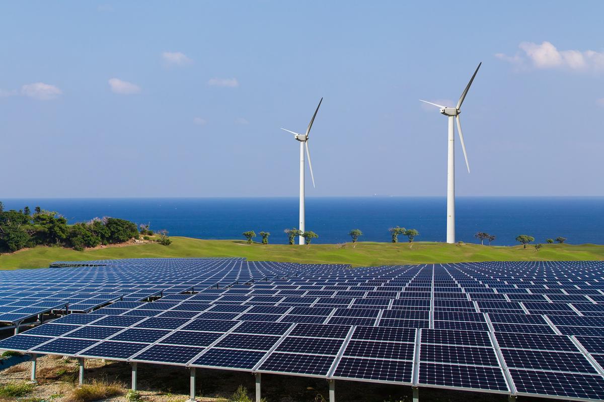 Una instalación de paneles fotovoltaicos compartiendo terreno con dos molinos eólicos.