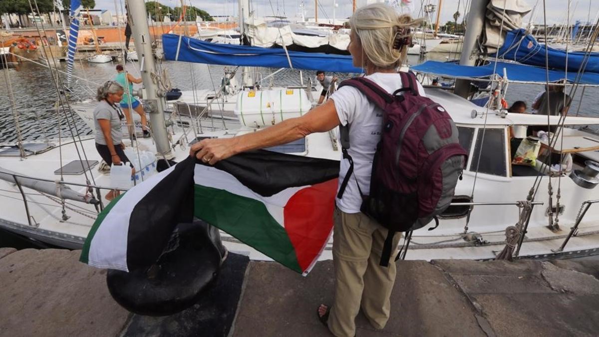 Una activista con la bandera palestina frente a uno de los dos veleros de la flotilla que ha partido hacia Gaza.