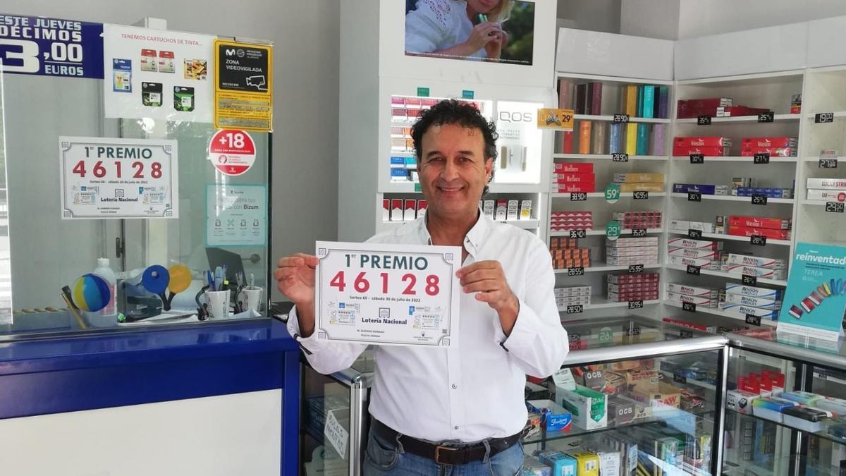 Damián Rubio, responsable del bazar El duende dorado, situado en la calle Mayor de Playa Honda,  muestra un cartel con el primer premio de lotería del sábado 30 de julio de 2022.