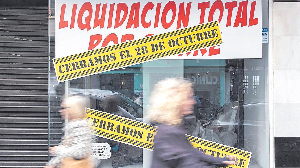 Dos personas pasan frente a una tienda en liquidación por cierre.