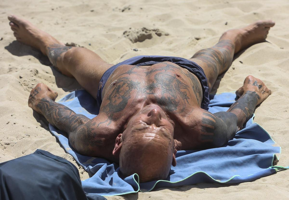 Un turista dormido al sol en una playa de la provincia de Alicante.