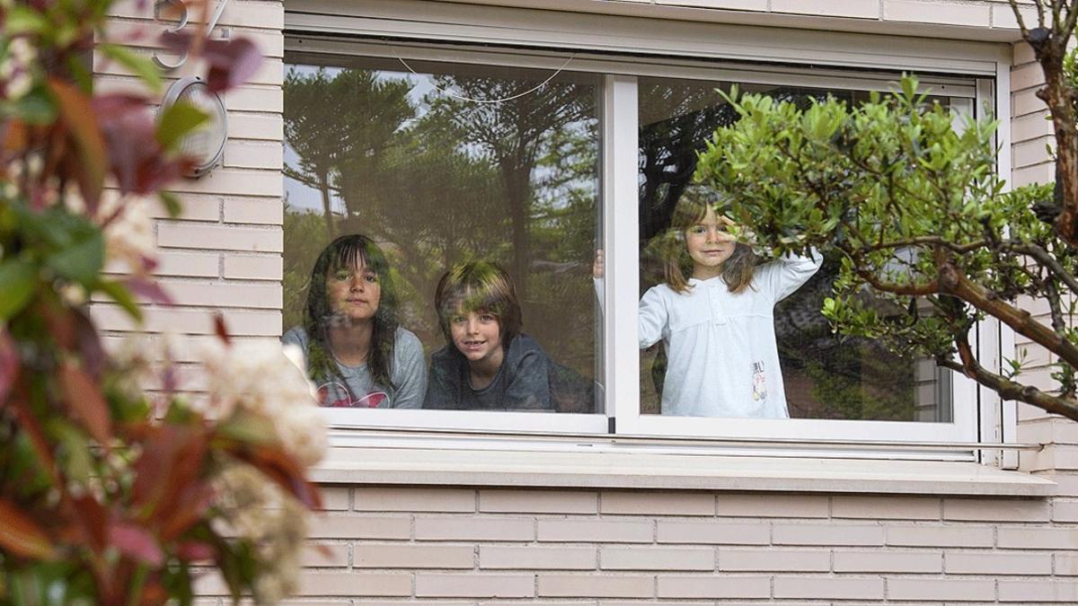 Tres hermanos de Igualada miran por la ventana de su casa durante el confinamiento, el pasado 21 de abril