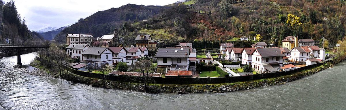 El poblado minero Bustiello, visto desde la orilla del río Aller por la que transita el trazado férreo.