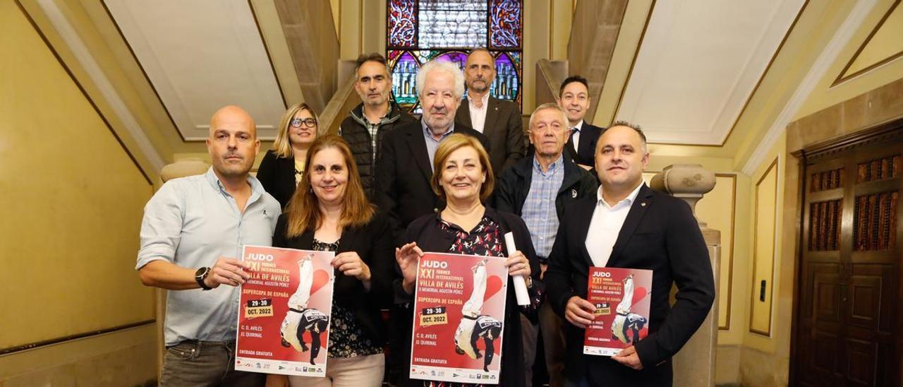 En primera fila, con los carteles, Carlos Fernández, Nuria Delmiro, concejala de Deportes; Mariví Monteserín, alcaldesa, y José Ramón Díaz Maseda, presidente de la Federación Asturiana. En segunda fila, Sara Retuerto, portavoz de Cambia Aviles; Javier Vidal, concejal no adscrito; y José Manuel García, «Roxín», presidente de la Unión de Comerciantes de Avilés y Comarca. En tercera fila, José Luis Ferrera, portavoz de Ciudadanos Avilés; Heriberto Menéndez, coordinador general de la Cámara de Comercio de Avilés y Daniel Rodríguez, presidente de Avilés Club de Empresas.