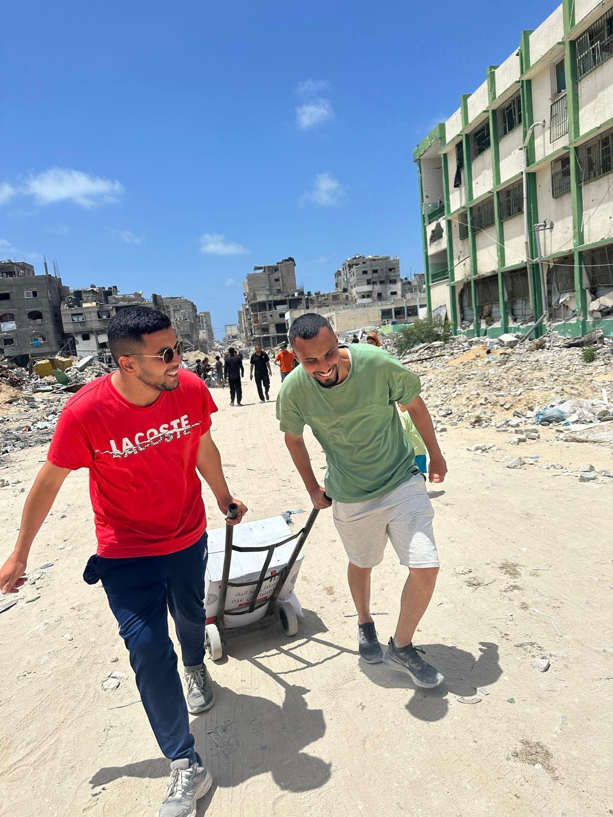 Abdalaziz, a la izquierda, tira de una carretilla con comida en medio de la destrucción de Gaza.
