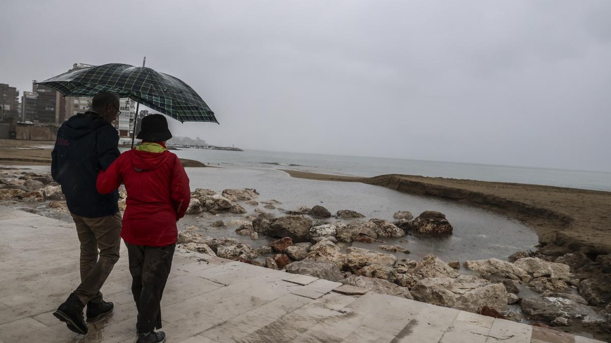 Dos personas observando los efectos de las lluvias en la playa de la Albufereta, en Alicante, hace unos días.