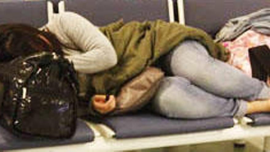 Una mujer duerme en un banco de la terminal del aeropuerto.