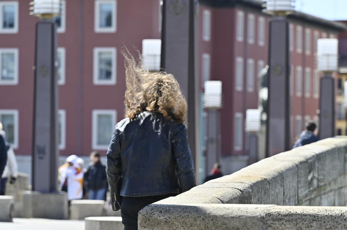 Una mujer camina por el puente de Piedra de Zaragoza con el viento levantándole el pelo