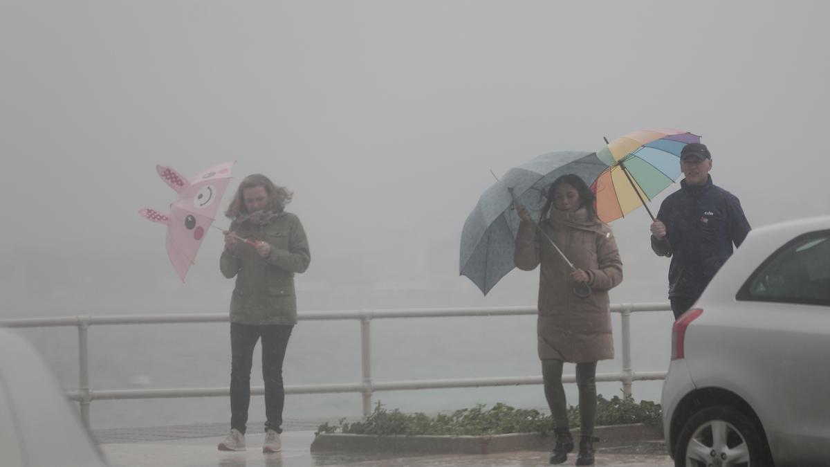 Tres ciudadanos se protegen de las fuertes lluvias con su paraguas