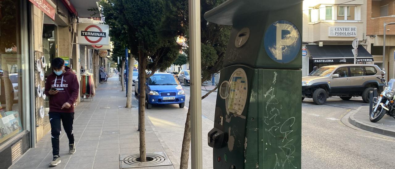 Un joven pasea por la acera al lado de un parquímetro en Benicarló.