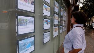 Una mujer mira en una inmobiliaria de Barcelona carteles de venta y alquileres de pisos.
