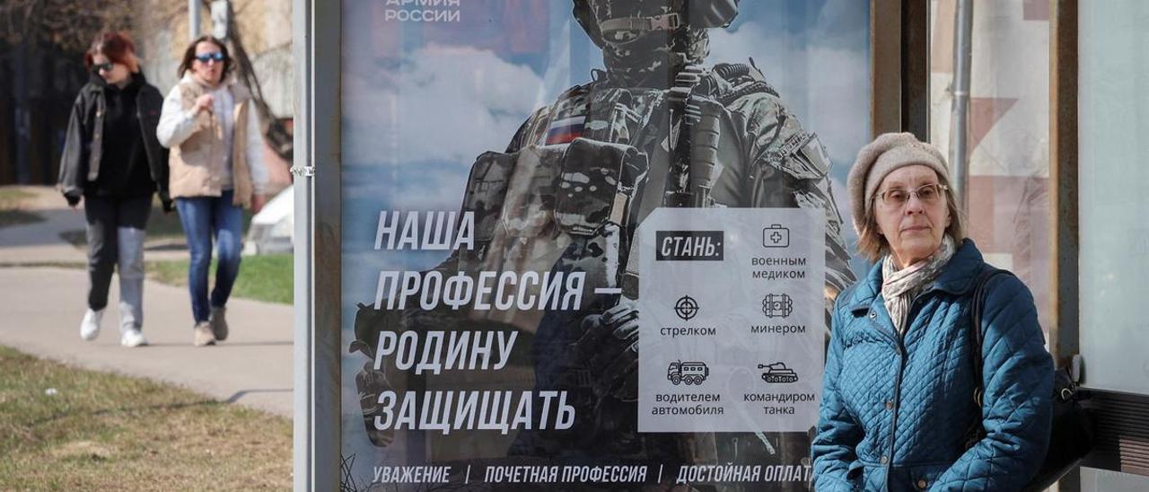 Una mujer espera el autobús junto a un póster que promociona el Ejército ruso, en Moscú.
