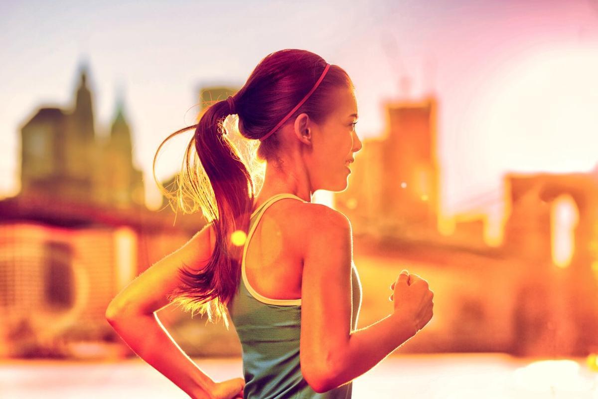 Running woman Asian runner in New York city sunset. Runner jogging in sunny bright light. Female fitness model training outside in New York City with skyline and Brooklyn Bridge in background.