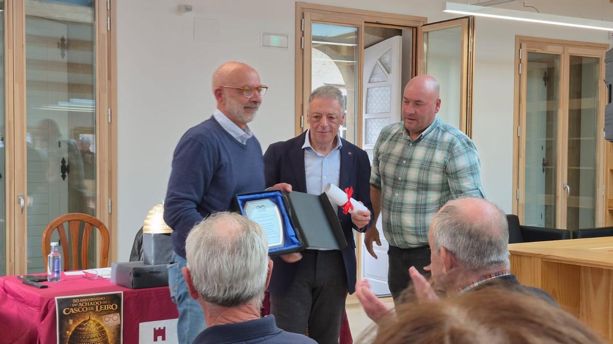Ángel Acuña, esquerda, viúvo da arqueóloga Rosa María Paz Lobeiras, recibindo a placa de mans de Xusto Ordóñez e Julio Alcalde.