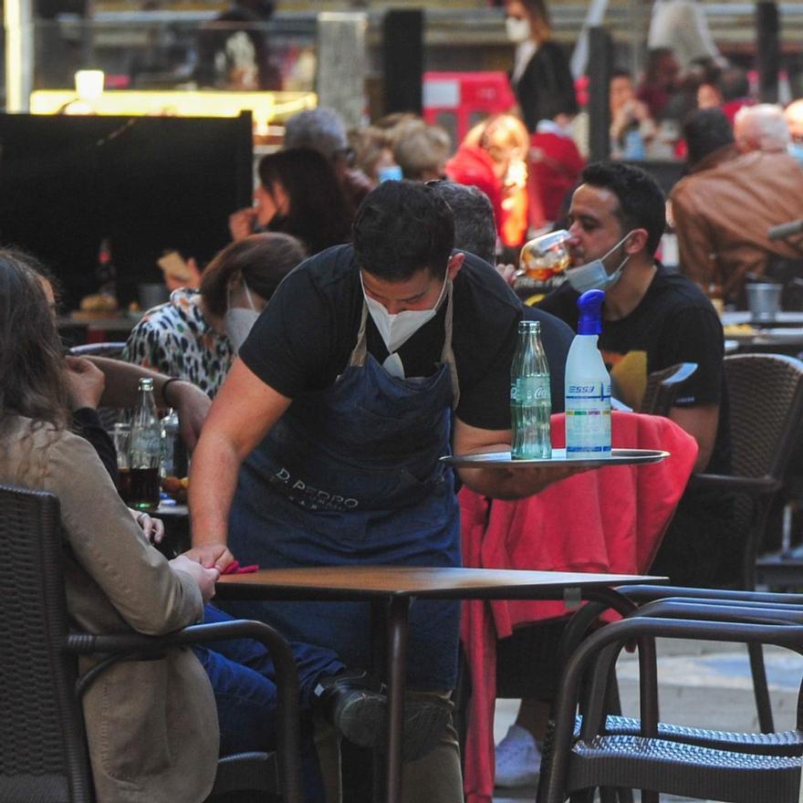 Un camarero con mascarillas limpiando una mesa tras desinfectarla.