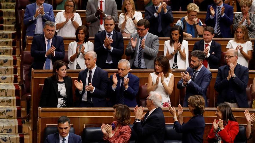 Pedro Sánchez, sentado, mientras su grupo aplaude alrededor.