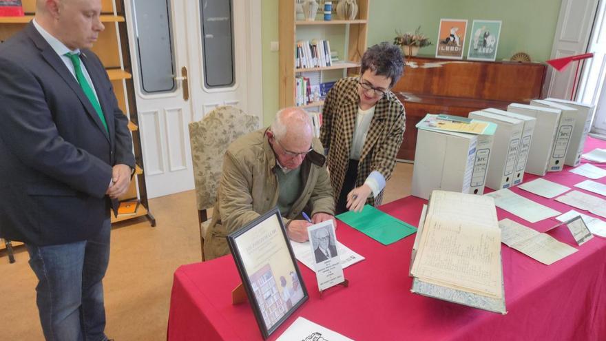 Vicente Loriente firma el documento de cesión de los documentos (expuestos en la mesa) en presencia del alcalde de Castropol y la bibliotecaria, Manuela Busto. | T. Cascudo