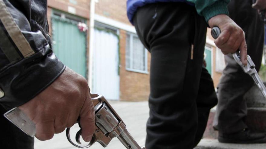 Tres personas sostienen sendas armas en una imagen de archivo tomada en Bogotá.