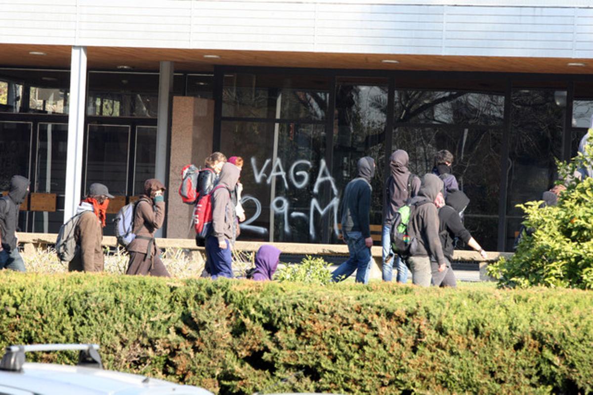 Estudiants passen davant d’un edifici amb una pintada de suport a la vaga.