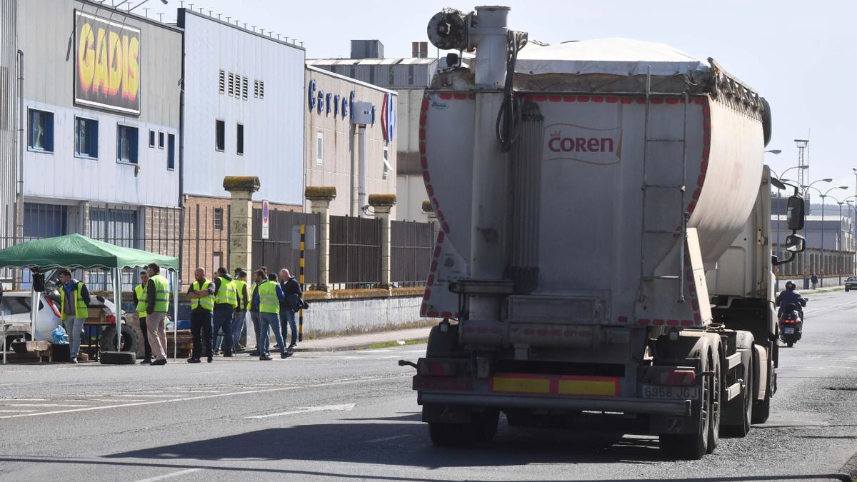 Un camión con cereales sale del puerto de A Coruña, con un piquete al fondo.