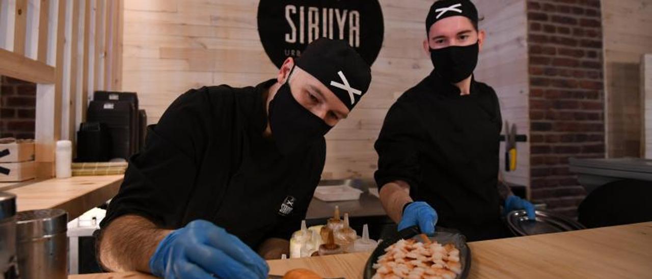 Dos trabajadores del Sibuya Urban Sushi Bar mostrando dos bandejas de sushi en el nuevo local.   | // GUSTAVO SANTOS