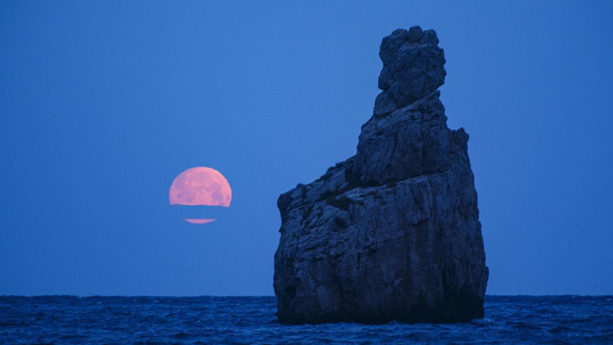 La luna se pone en el horizonte junto al Carall Bernat durante un amanecer en Cala Benirràs.