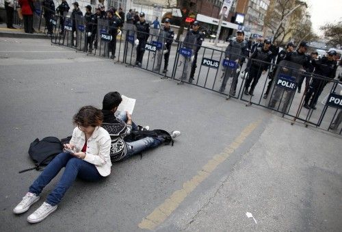 Protester reads a book and another uses her smartphone as they wait in front of a police barricade on a road leading to the Supreme Electoral Board in Ankara