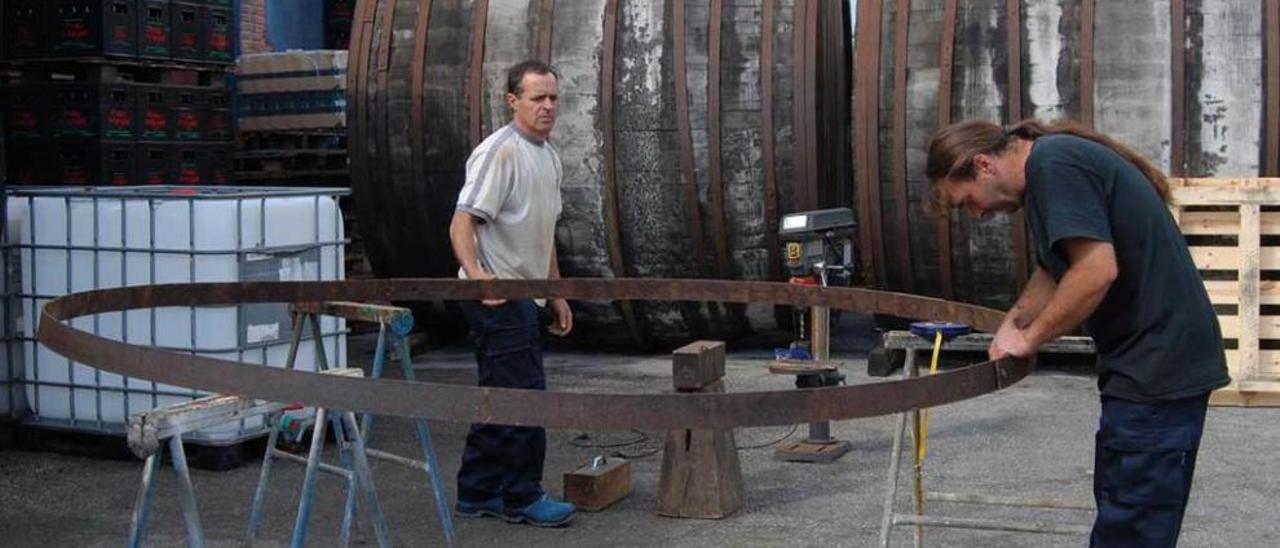 Emilio García y Carlos Argüelles miden el aro de uno de los toneles para ajustarlo, en Nava.