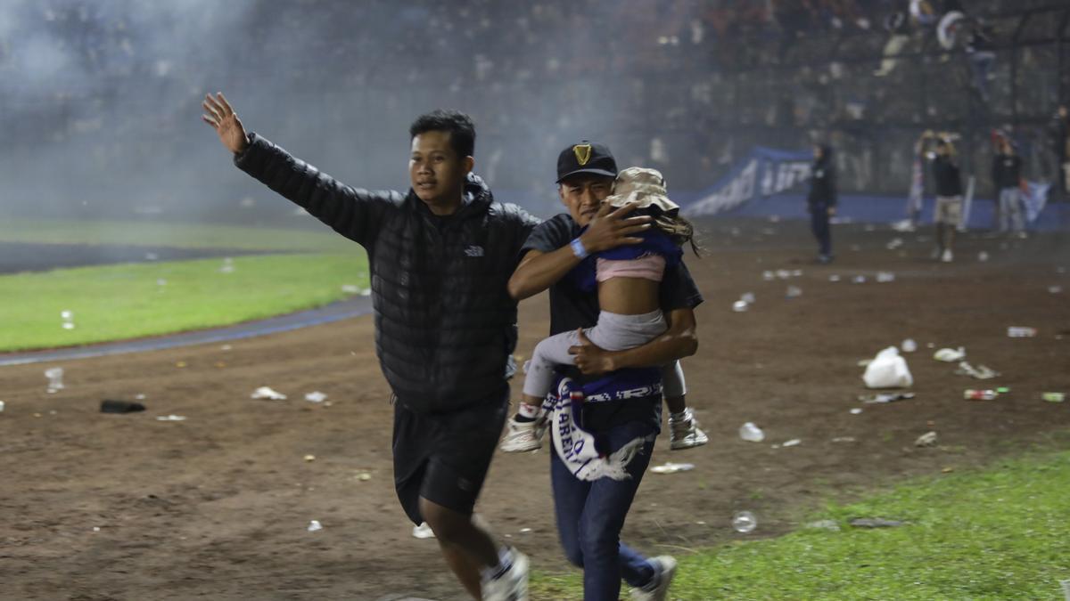 Aficionados del Arema intentan evacuar el campo con un niño.