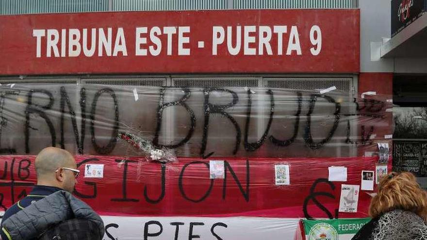 Dos aficionados observan el altar en recuerdo de Quini en la puerta 9 instaurado tras su fallecimiento.