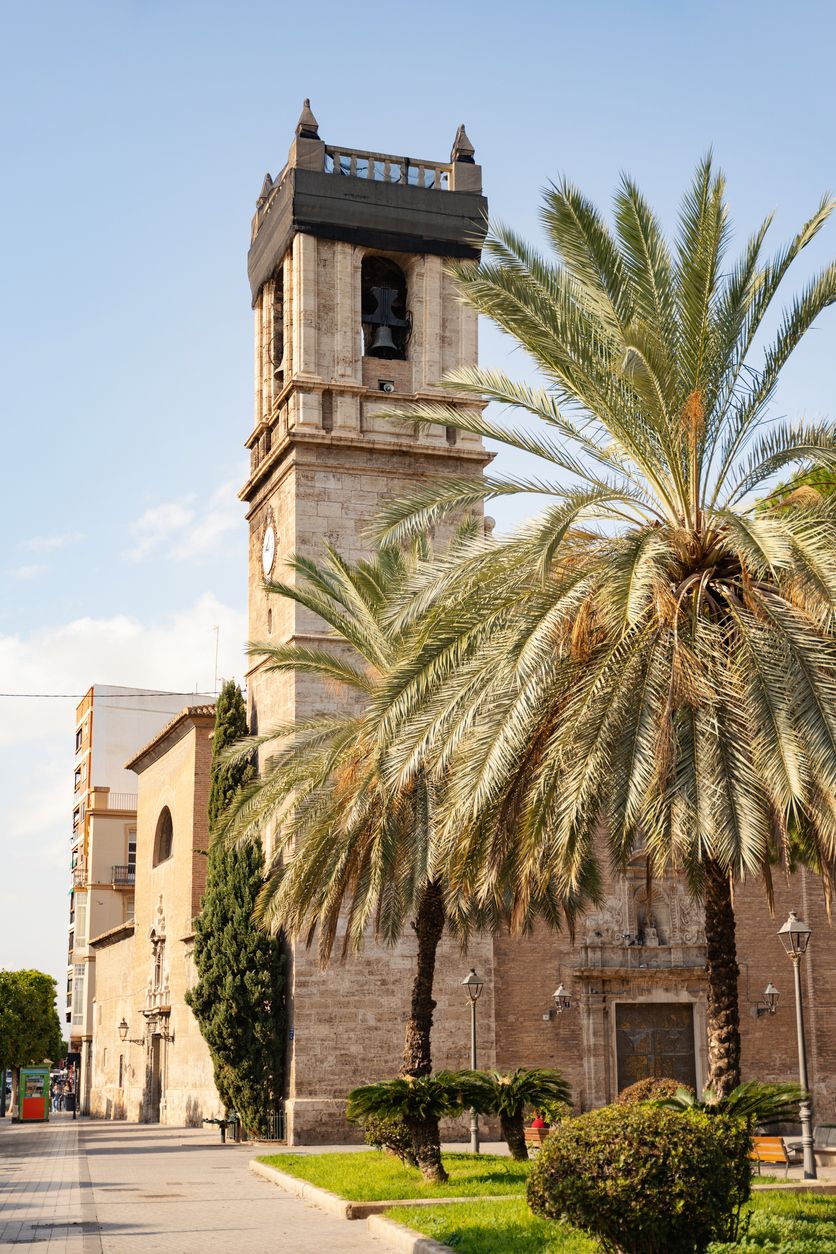 Vista de la Basílica de Santa María de La Nucía con enormes palmeras al frente.