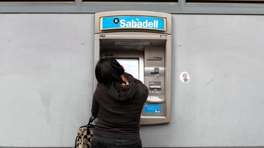 Una mujer saca dinero de un cajero del Sabadell.