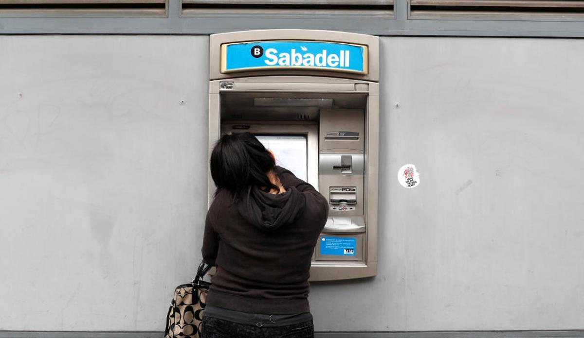 Una mujer saca dinero de un cajero del Sabadell.