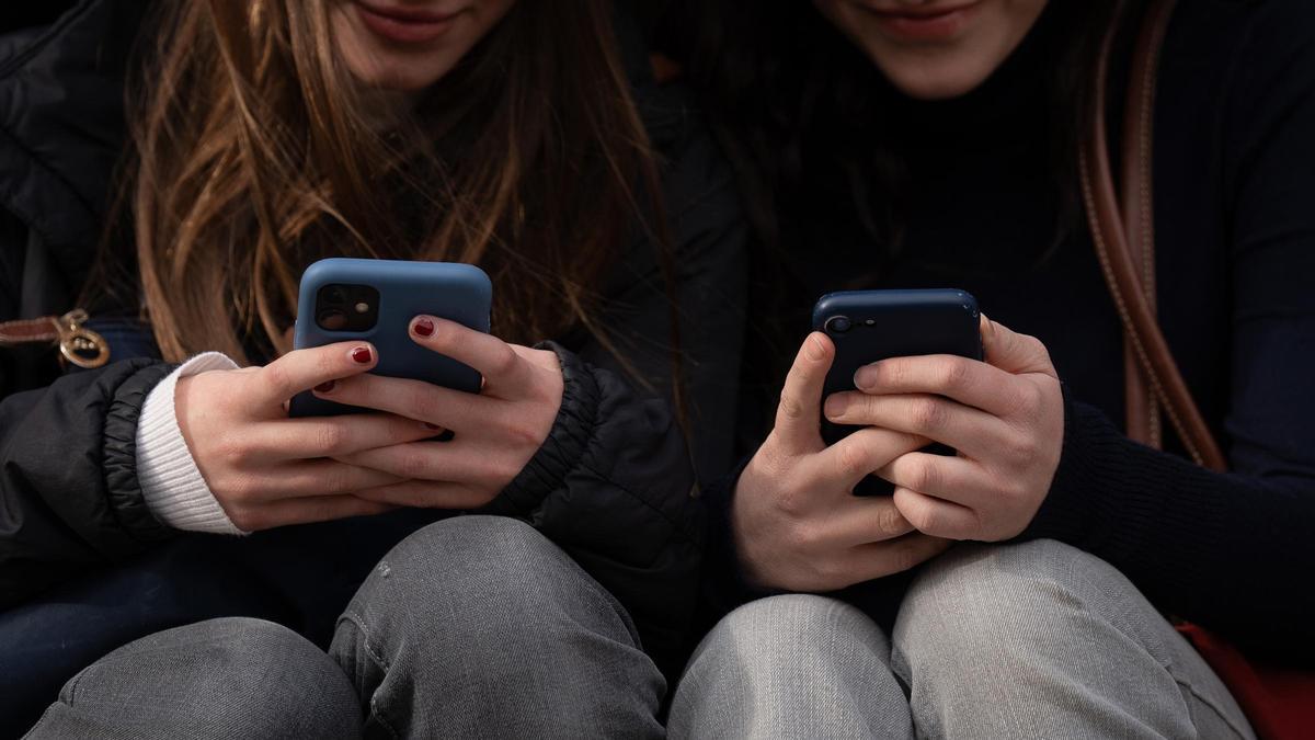 Dos jóvenes miran sus teléfonos móviles.